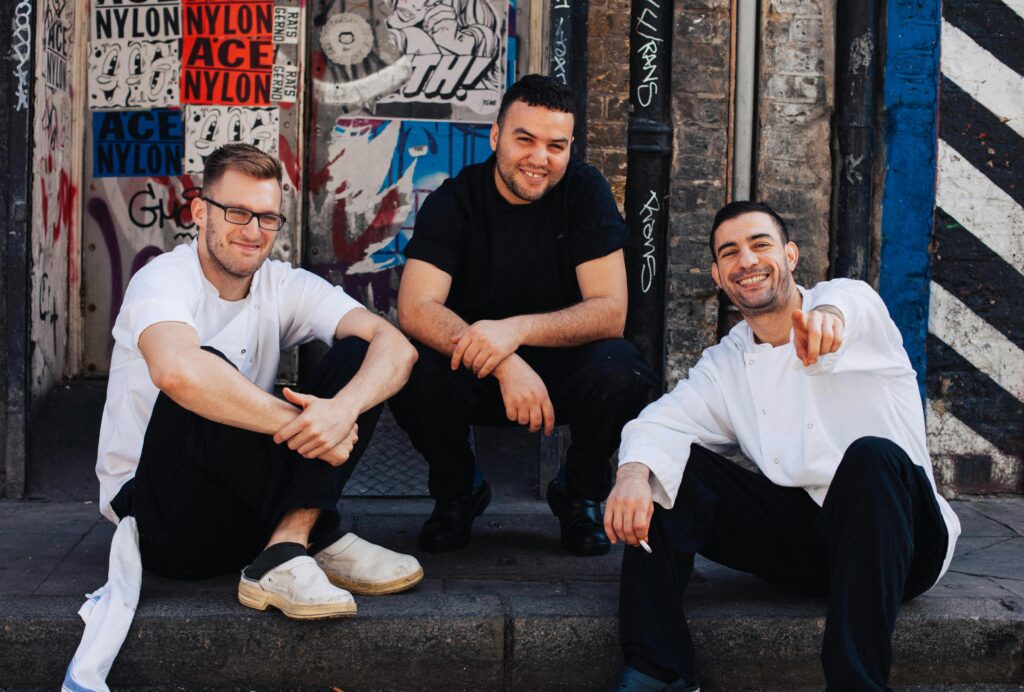 Three men sitting in front of urban street art, enjoying a casual moment together.